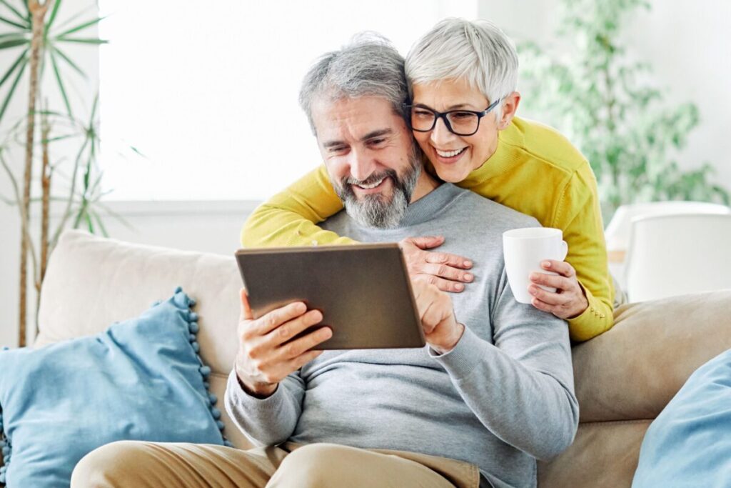 Older couple smiling while looking at a tablet together, reflecting on the question: is it time for senior living?