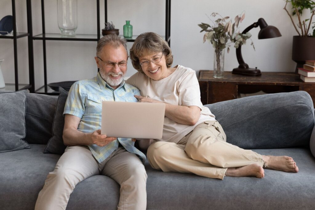 Questions to ask before choosing senior living as a couple reviews information together on a laptop while sitting comfortably on a sofa in a relaxed home setting.
