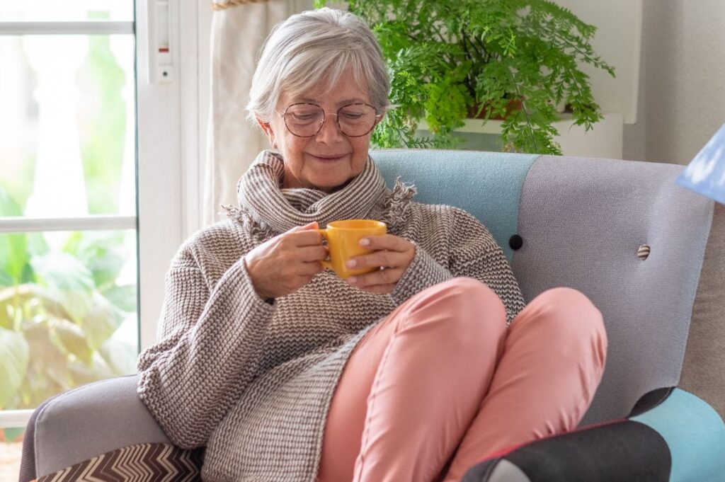 Older woman relaxing comfortably in a chair with a warm drink, reflecting signs it’s time for assisted living.