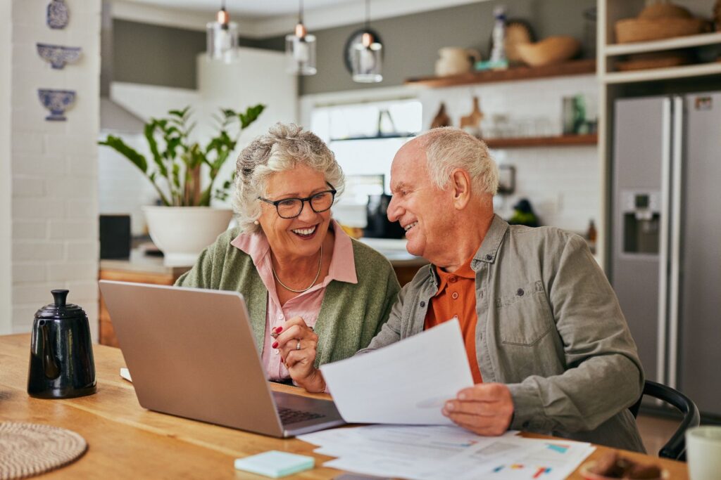 A smiling older couple reviews documents together at their kitchen table, enjoying the ease and comfort of independent living in Hendersonville.